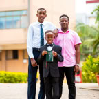 A joyful family portrait of three men celebrating a graduation outdoors in a sunny setting.